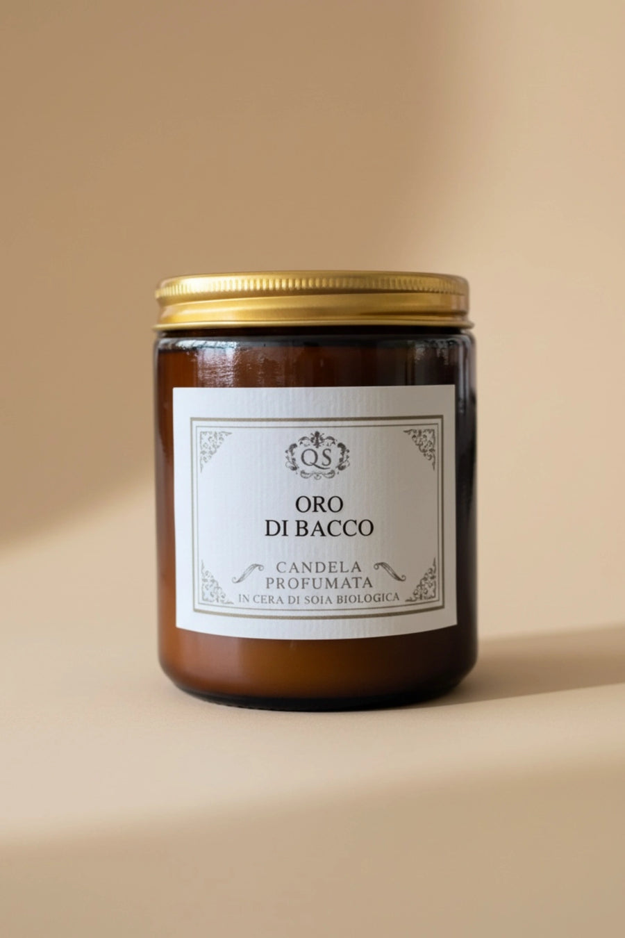 Candela profumata Oro di Bacco in vetro ambrato con tappo dorato su sfondo beige