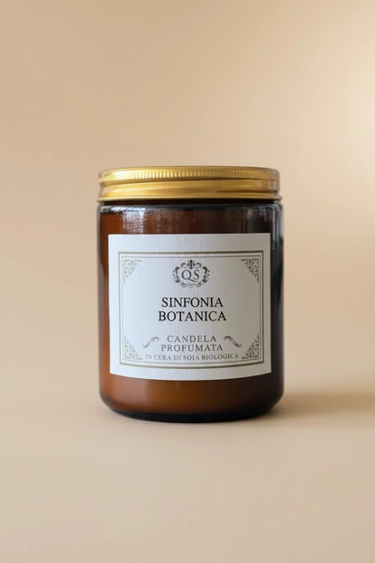 Candela profumata alla soia Sinfonia Botanica in vetro ambrato con tappo dorato su sfondo beige